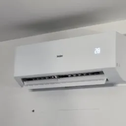 Biały klimatyzator Haier zamontowany na jasnej ścianie, wyświetlający temperaturę 28 stopni Celsjusza.