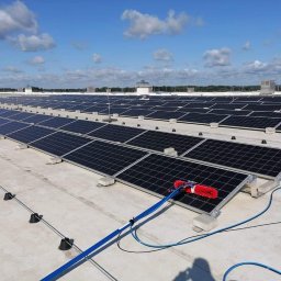 ELEPHANT CLEAN M&K - Czyszczenie paneli słonecznych na dachu budynku przemysłowego za pomocą szczotki z doprowadzeniem wody pod ciśnieniem, błękitne niebo z chmurami w tle.