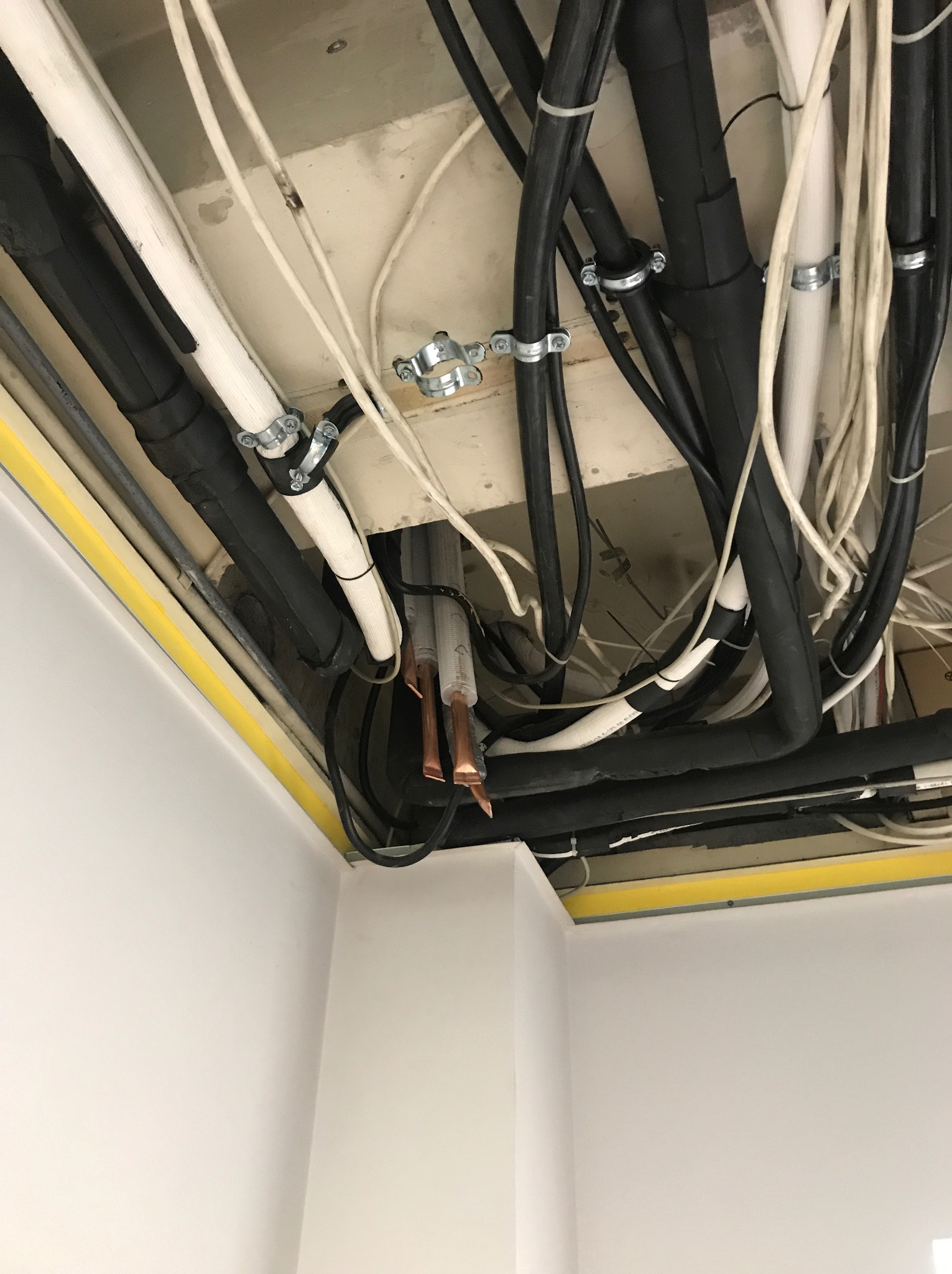 Instalacja rur i przewodów pod sufitem podwieszanym z widocznymi miedzianymi końcówkami, mocowane metalowymi obejmami i opaskami zaciskowymi.