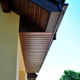 epodbitki.pl - Nowoczesne podbitki dachowe z ciemnego drewna, widok z dołu, jasne niebo w tle, fragment rynny.