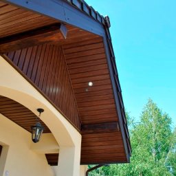 epodbitki.pl - Drewniana podbitka dachowa z oświetleniem punktowym, widok z dołu na jasnym tle nieba i drzew, z elementami elewacji budynku.