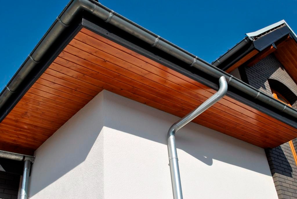 Nowoczesny dom z drewnianą podbitką i metalowymi rynnami w kolorze grafitowym, uchwyconymi w słoneczny dzień.