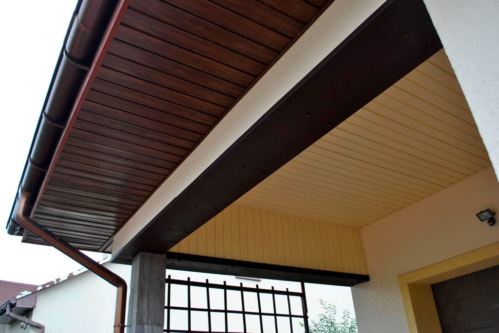 Zadaszenie wejścia z brązową drewnopodobną podbitką i miedzianą rynną, widok z dołu.