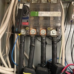 Dariusz Miodek MaxSerwis - Rozdzielnica elektryczna z widocznymi przewodami, bezpiecznikami i elementami sterującymi. Detal instalacji elektrycznej z bliska, widoczne oznaczenia i kable.