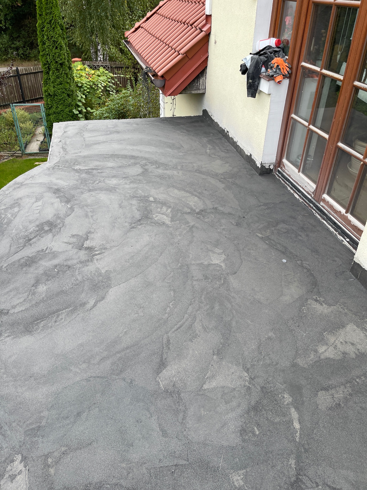 Szara, płaska powierzchnia balkonu po renowacji, widoczne ślady farby, w tle okno i narzędzia pracy.