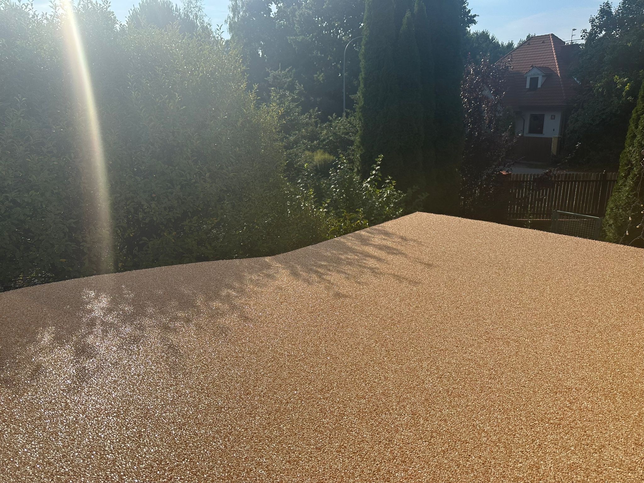 Balkon z nową, beżową, żywiczną posadzką, widok na zieleń i dom w tle, mocne światło słoneczne.