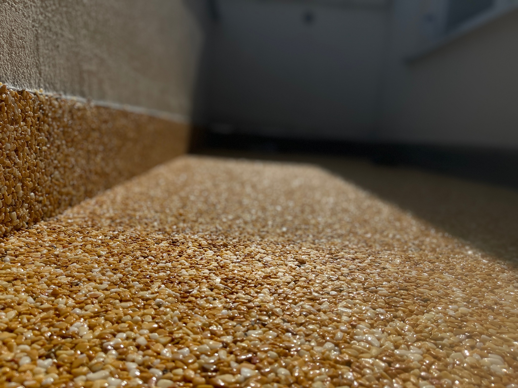 Balkon wykończony żywicą epoksydową z drobnymi kamyczkami w odcieniach beżu i brązu, widok z niskiej perspektywy podkreślający strukturę powierzchni.