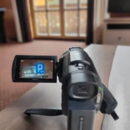 Kamera Sony na statywie nagrywa znak drogowy zakazu parkowania wewnątrz budynku z drewnianymi oknami w tle.