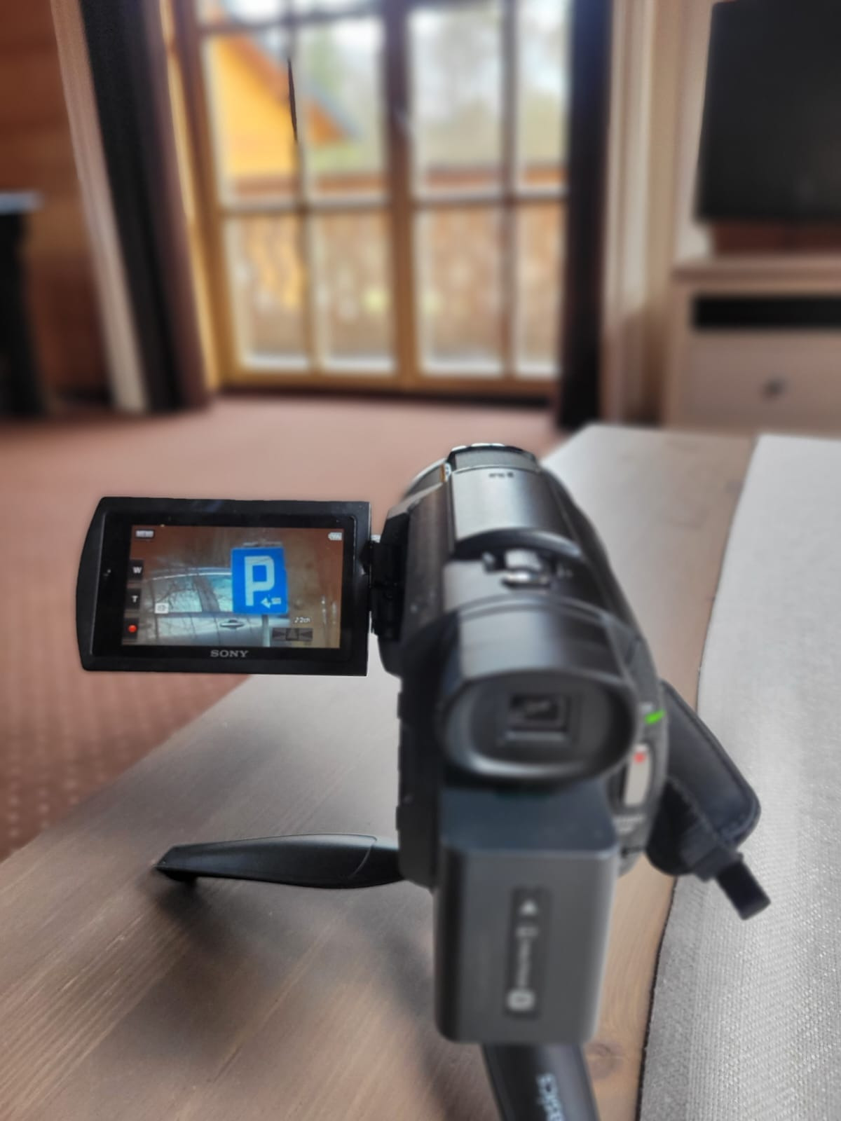 Kamera Sony na statywie nagrywa znak drogowy zakazu parkowania wewnątrz budynku z drewnianymi oknami w tle.