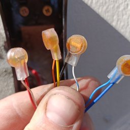 ART MUSIC OBSŁUGA MUZYCZNA IMPREZ LISZEWSKI ARKADIUSZ - Dłoń trzymająca złączki WAGO z przewodami w różnych kolorach na tle ściany i czarnej obudowy. Widoczne detale połączeń elektrycznych.