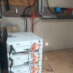 ART MUSIC OBSŁUGA MUZYCZNA IMPREZ LISZEWSKI ARKADIUSZ - Bateria litowo-jonowa Deye SE-G5.1 Pro-B, trzy moduły ułożone jeden na drugim, podłączone do instalacji elektrycznej z przewodami w kolorach czerwonym, czarnym i żółto-zielonym.