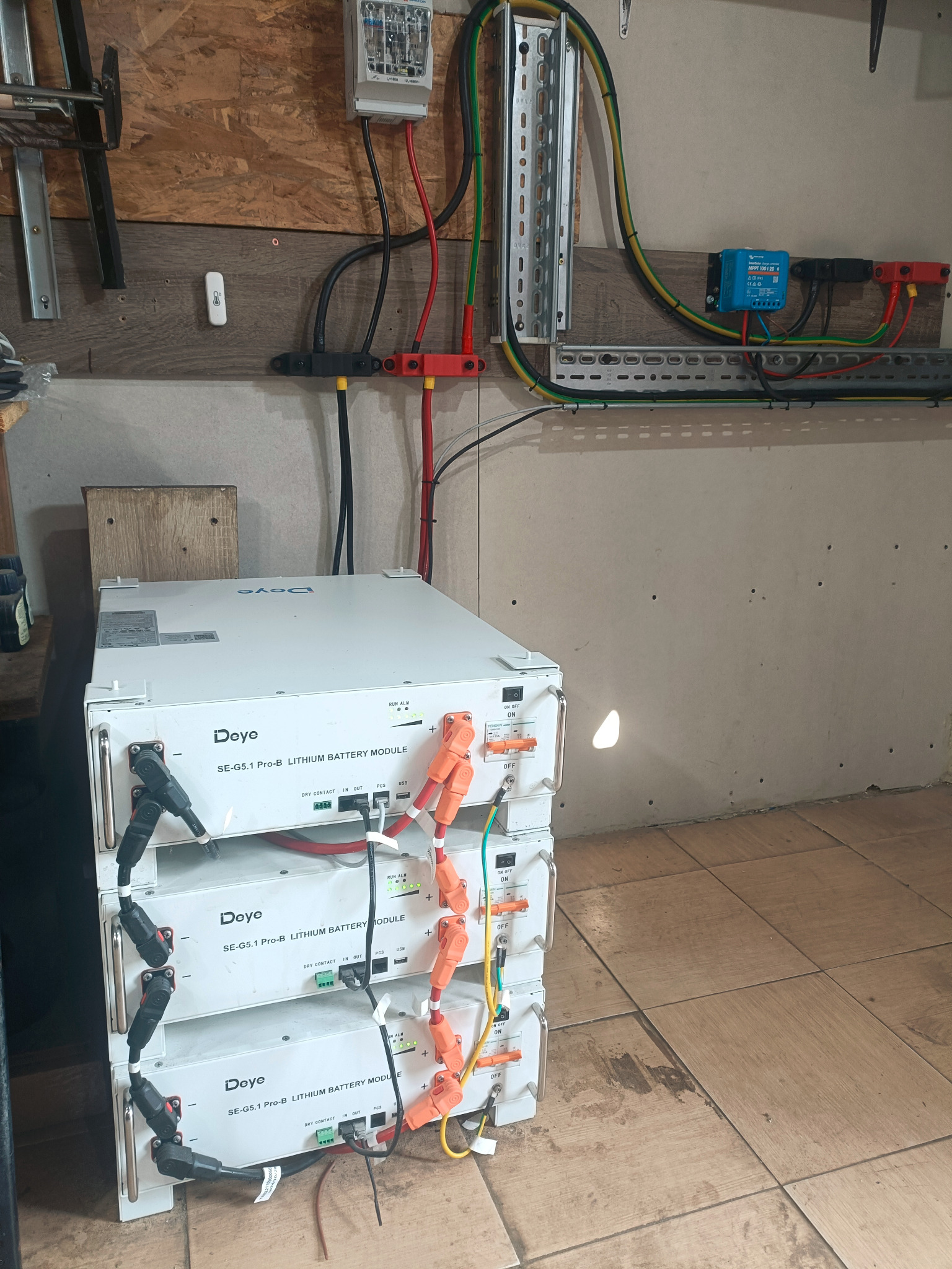 Bateria litowo-jonowa Deye SE-G5.1 Pro-B, trzy moduły ułożone jeden na drugim, podłączone do instalacji elektrycznej z przewodami w kolorach czerwonym, czarnym i żółto-zielonym.