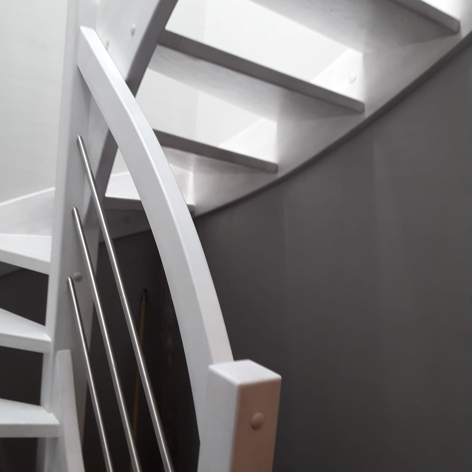 Białe schody z metalowymi balustradami, widok z dołu, szara ściana w tle.