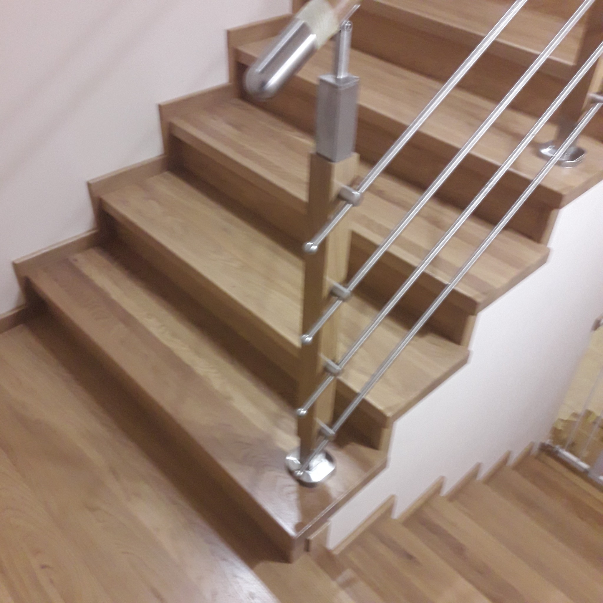 Jasne, drewniane stopnie schodów z metalową, nowoczesną balustradą z poziomych prętów, widok z góry.