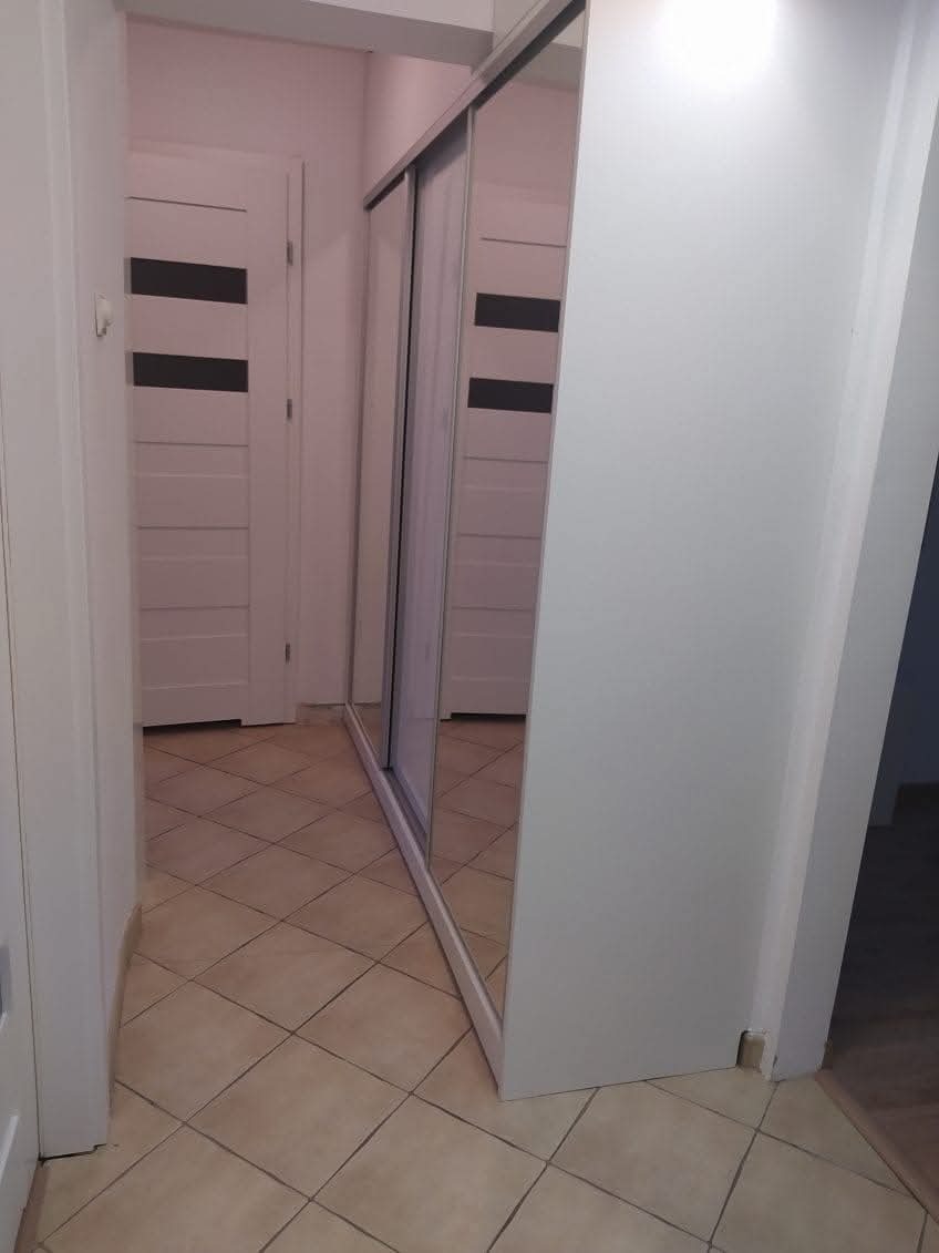 Biała szafa przesuwna z lustrami w przedpokoju z beżową podłogą z płytek i białą ścianą oraz widocznymi białymi drzwiami w tle.