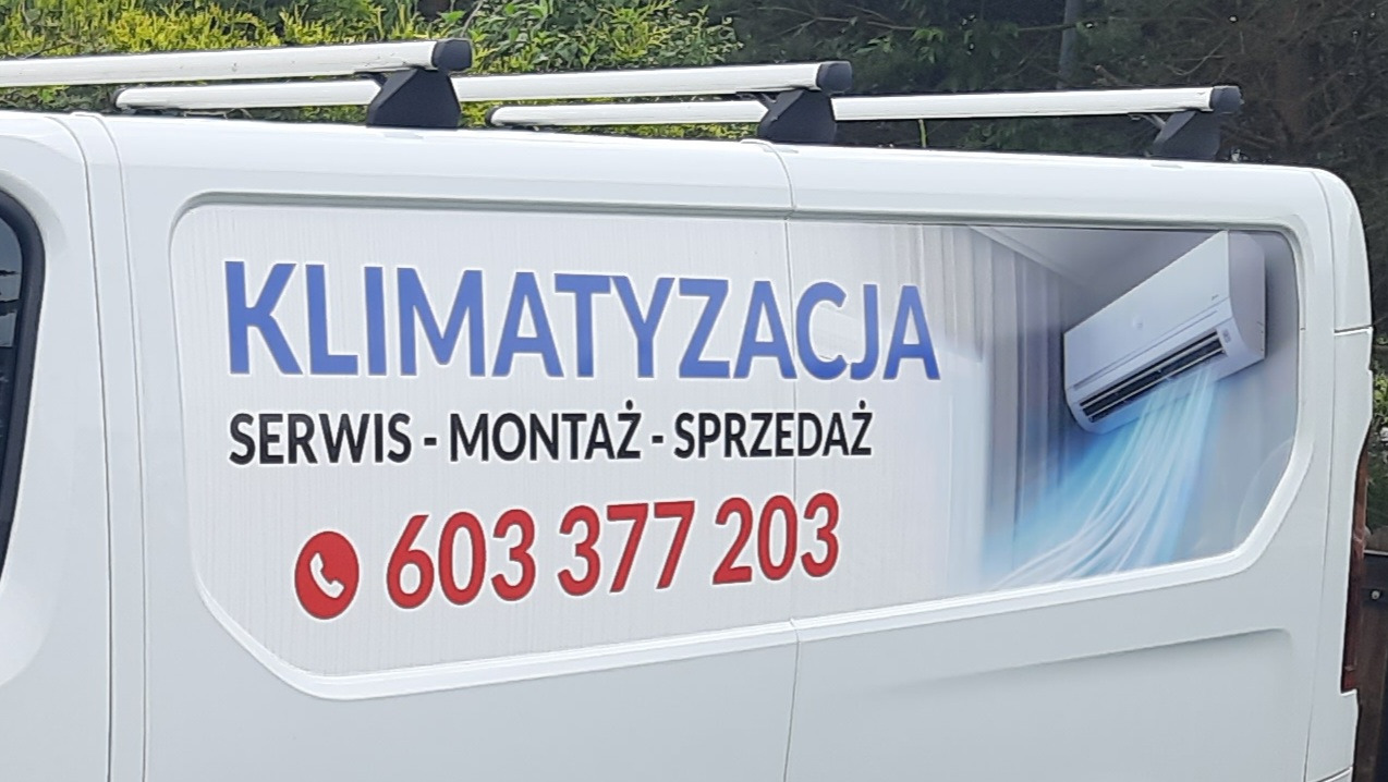Biały samochód z reklamą: klimatyzacja, serwis, montaż, sprzedaż i numer telefonu. Widoczny klimatyzator z niebieskim strumieniem powietrza.