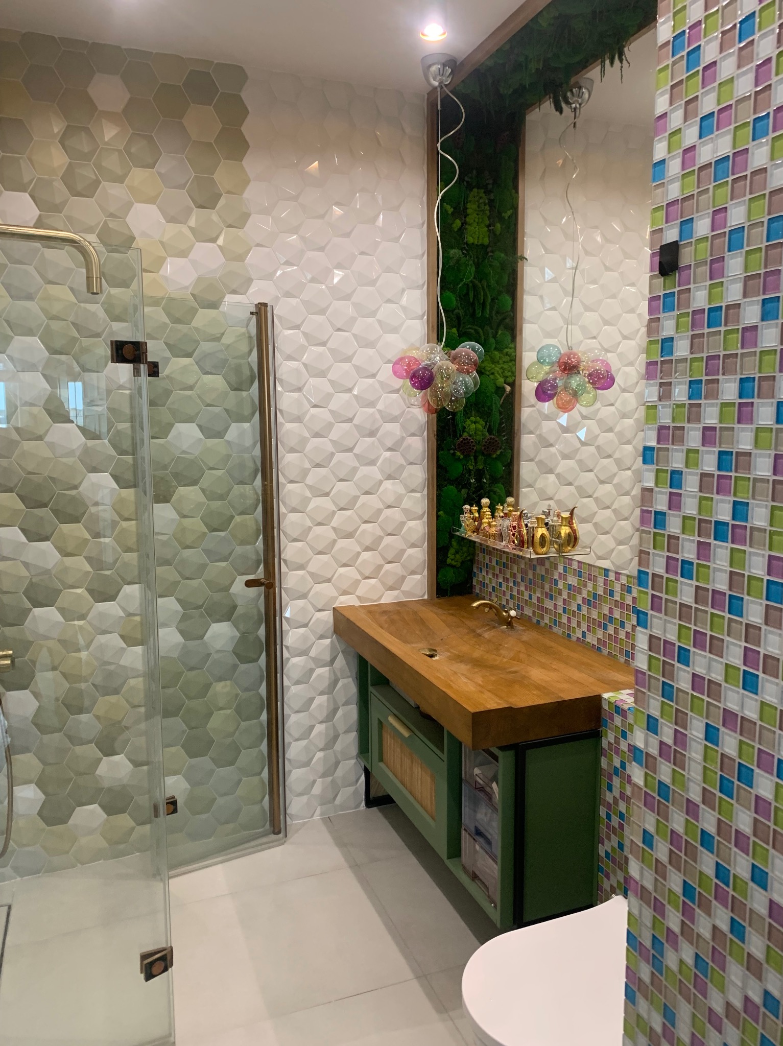 Nowoczesna łazienka z kabiną prysznicową, drewnianą umywalką na zielonej szafce i dekoracyjnymi płytkami mozaikowymi na ścianie, oświetlona lampami w kształcie kul.