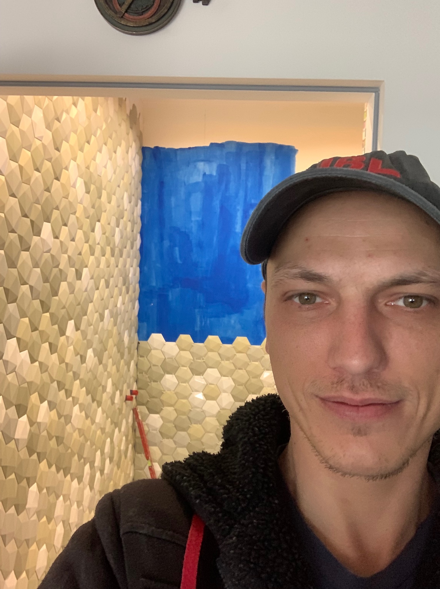 Mężczyzna na tle ściany z heksagonalnych płytek w odcieniach beżu i błękitu. Nietypowe wykończenie wnętrza w trakcie prac. Widoczny poziomica.