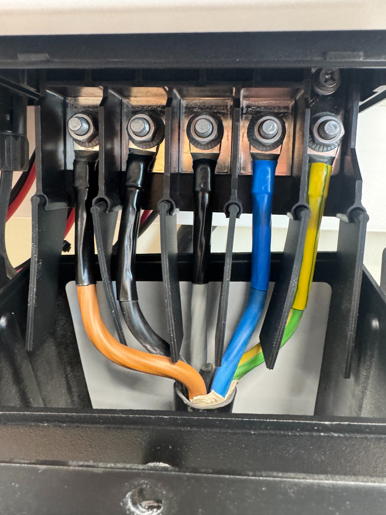 Szczegółowe ujęcie złącza elektrycznego z kolorowymi przewodami (pomarańczowy, czarny, niebieski, żółto-zielony) w instalacji fotowoltaicznej.