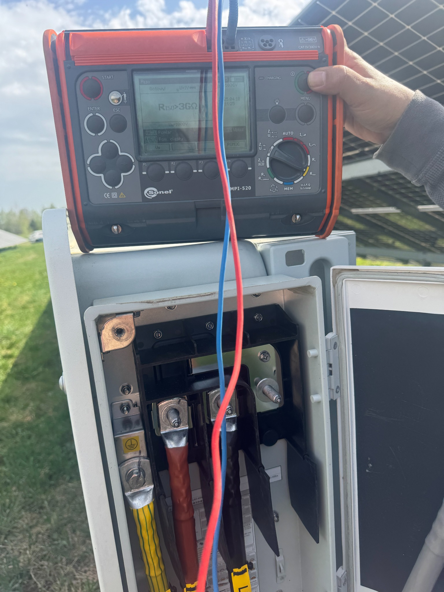 Pomiar rezystancji izolacji instalacji fotowoltaicznej miernikiem Sonel MPI-520 w rozdzielnicy, widoczne kable pomiarowe i panele w tle.