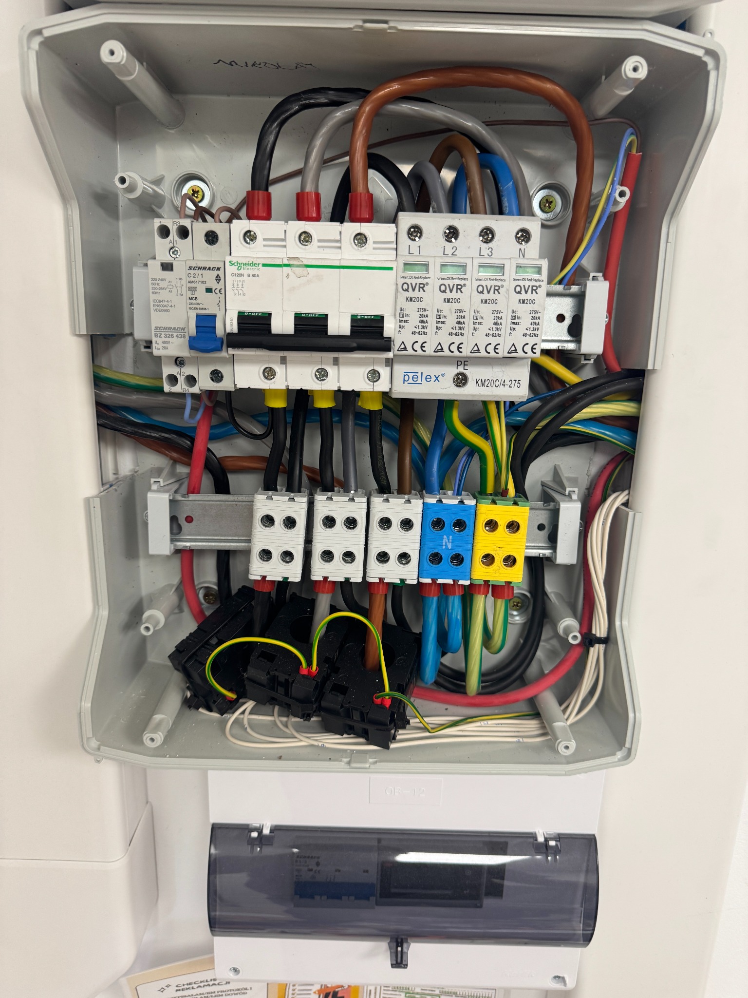 Otwarta skrzynka z zabezpieczeniami fotowoltaicznymi: bezpieczniki, przewody w kolorach, listwy zaciskowe. Widoczne oznaczenia L1, L2, L3 i N.