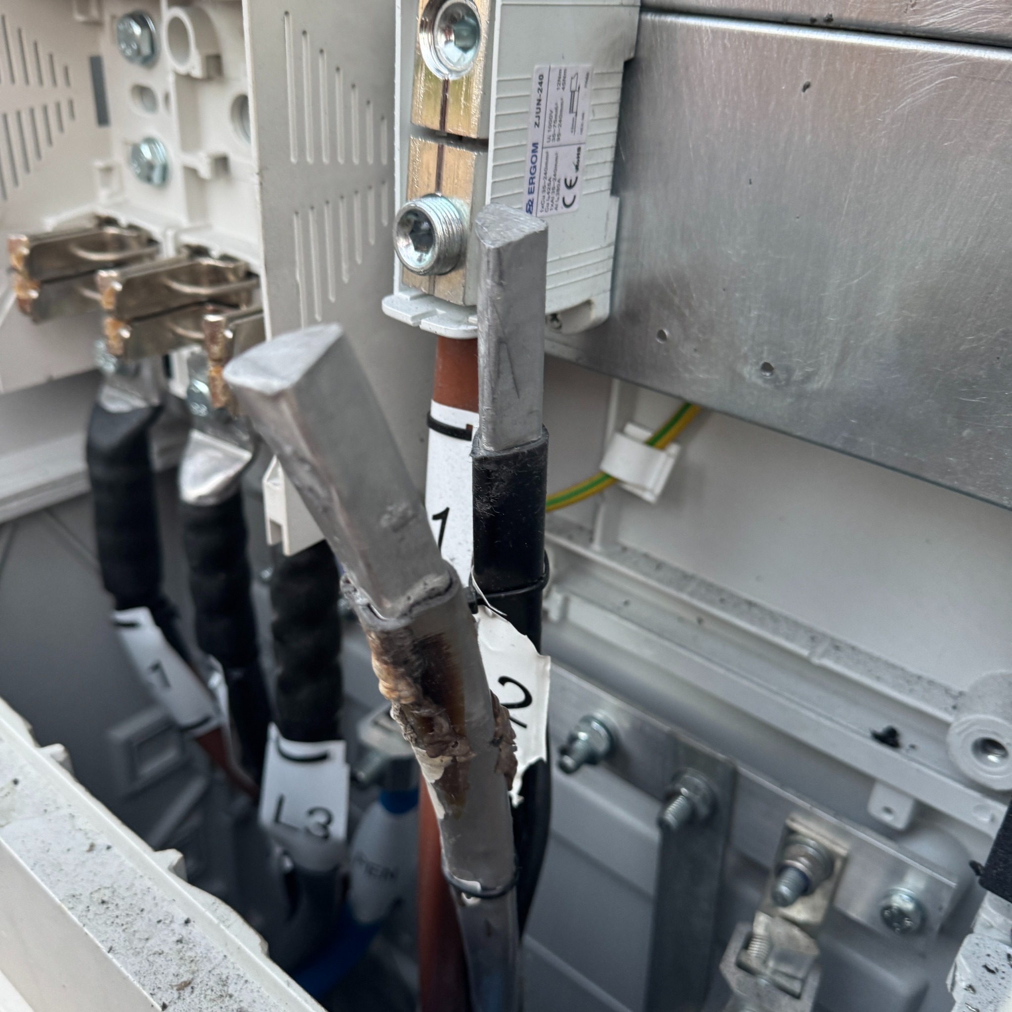 Szczegółowe ujęcie podłączenia kabli oznaczonych L1, L2, L3 w skrzynce instalacji fotowoltaicznej. Widoczne śruby, przewody i oznaczenia na kablach.