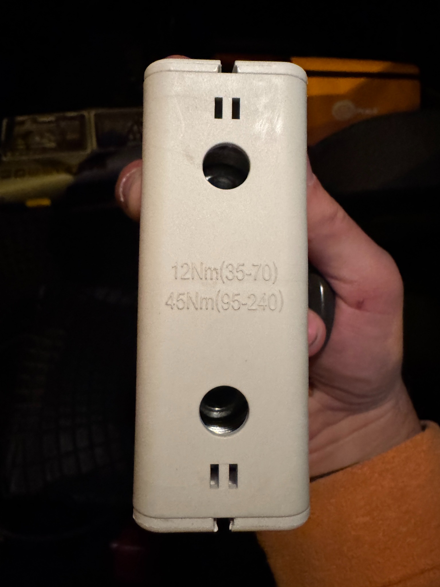 Biała obudowa z otworami i oznaczeniami momentu obrotowego trzymana w dłoni, prawdopodobnie element instalacji fotowoltaicznej w trakcie serwisu.