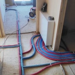 Oleksandr Borodavkin - Instalacja ogrzewania podłogowego w trakcie montażu z widocznymi rurami w kolorach czerwonym i niebieskim, prowadzonymi po szlichtcie, przymocowanymi opaskami, z rozdzielaczem na ścianie...