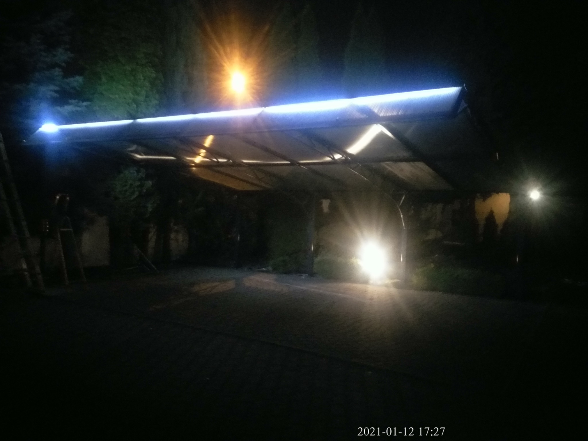 Zadaszenie z blachy trapezowej oświetlone listwą LED, widoczne w nocy, z przodu jasne światło samochodu.