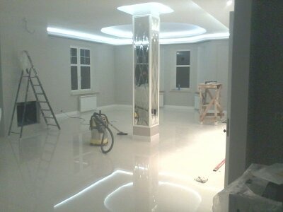 Wnętrze po odnowieniu: świeżo pomalowane ściany w odcieniach szarości, błyszcząca podłoga, kolumna z lustrzanymi panelami, oświetlenie LED w suficie, drabina i odkurzacz w rogu pomieszczenia.