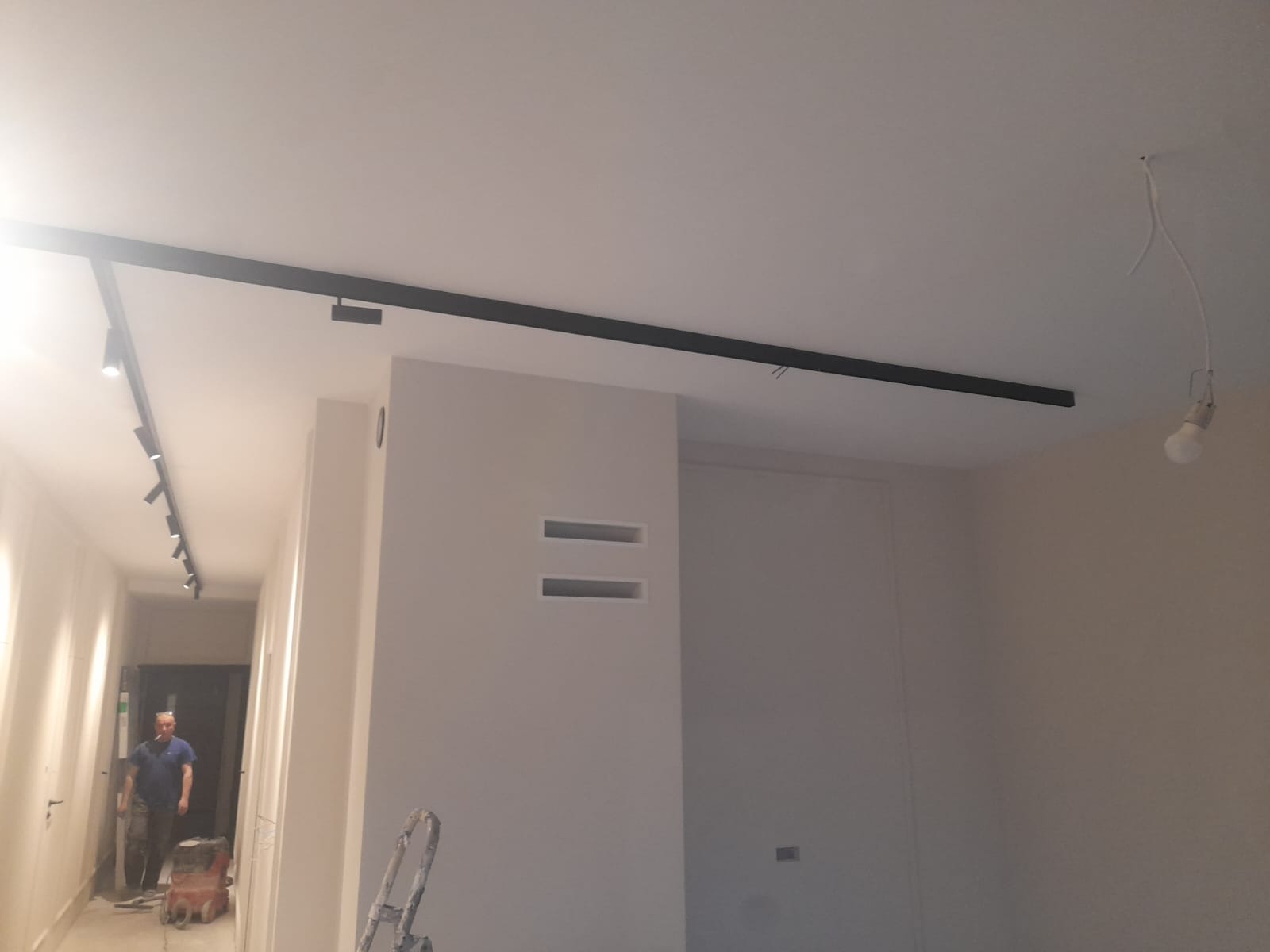 Nowoczesny system szynowy z reflektorami w świeżo pomalowanym wnętrzu, widoczna drabina malarska i elektryk z narzędziami w tle.