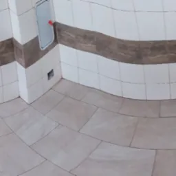 Panoramiczne ujęcie wnętrza w trakcie prac wykończeniowych, widoczne ułożone płytki podłogowe i ścienne z dekoracyjnym pasem, wystające rury instalacji, przygotowane miejsce na otwór rewizyjny...