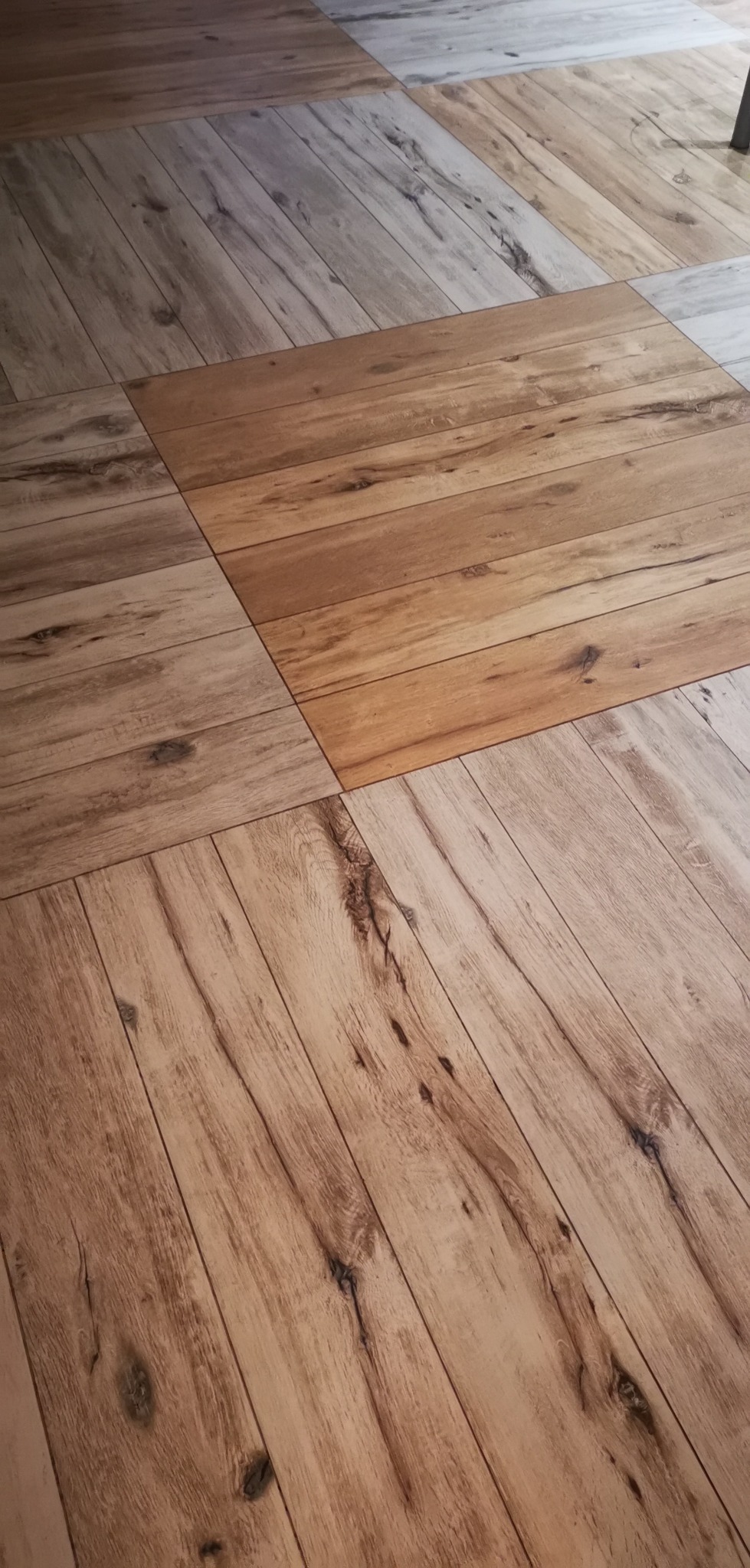 Ułożone panele podłogowe w odcieniach brązu i szarości, z widoczną strukturą drewna i naturalnymi usłojeniami, tworzące geometryczny wzór.