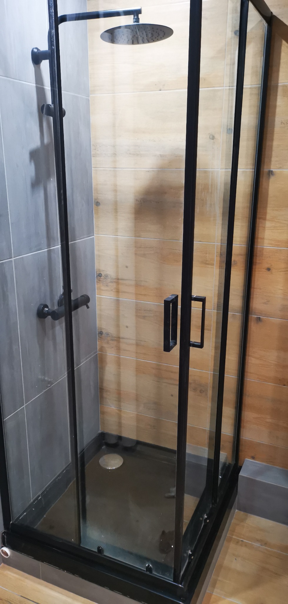 Kabina prysznicowa z czarnymi ramami i deszczownicą, na ścianach szare i drewnopodobne płytki.