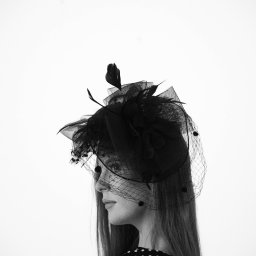 STUDIO KREATYWNE Katarzyna Ćwiertnia - Czarno-białe portretowe ujęcie kobiety z profilu, noszącej elegancki czarny kapelusz z woalką i piórami, w bluzce w białe kropki na czarnym tle.