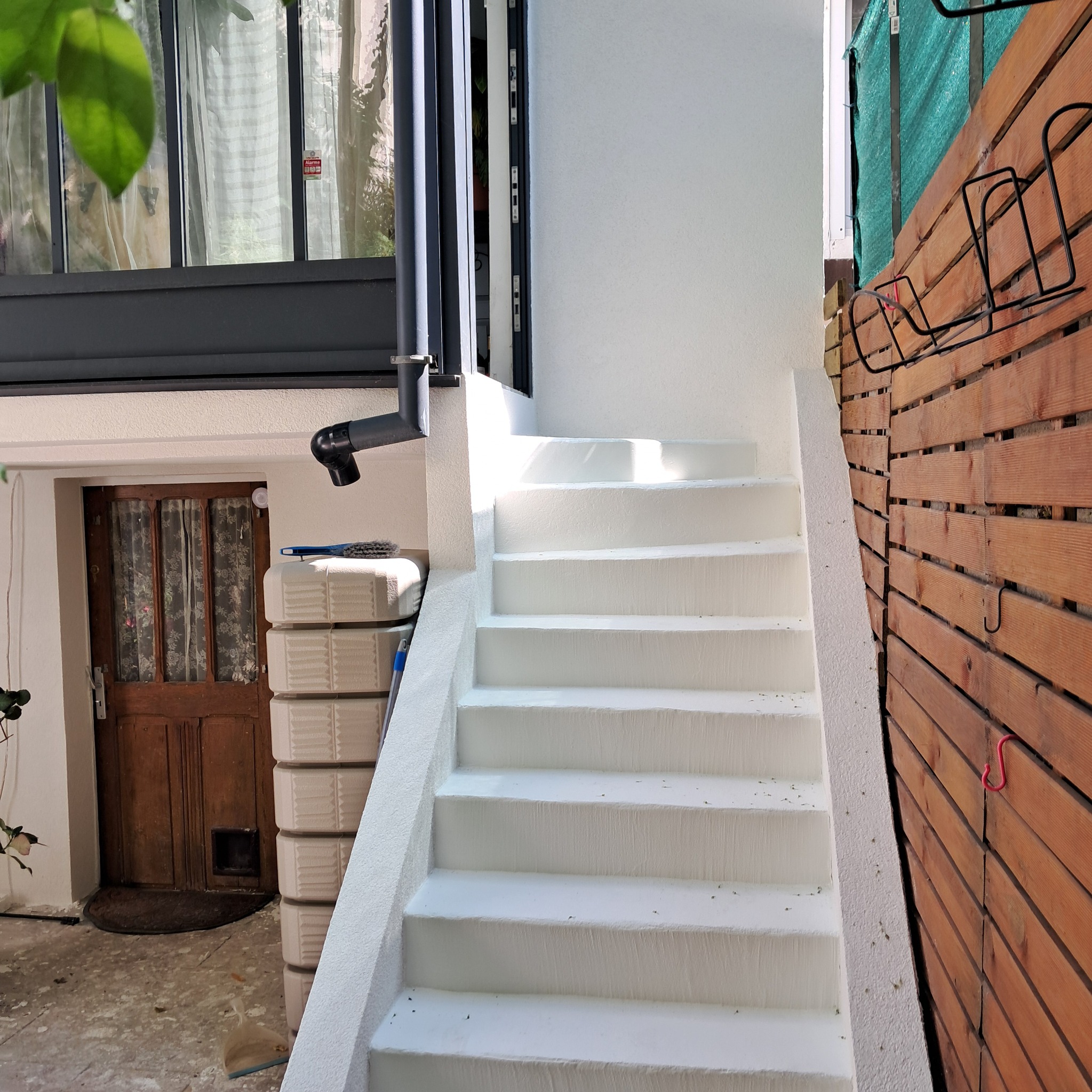 Białe schody zewnętrzne po renowacji, prowadzące w górę przy drewnianej elewacji. Widoczny fragment okna i drzwi wejściowych w tle.