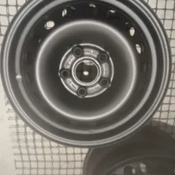 Dwie stalowe felgi samochodowe po piaskowaniu, leżące na siatce, z widocznymi otworami i oznaczeniami producenta.