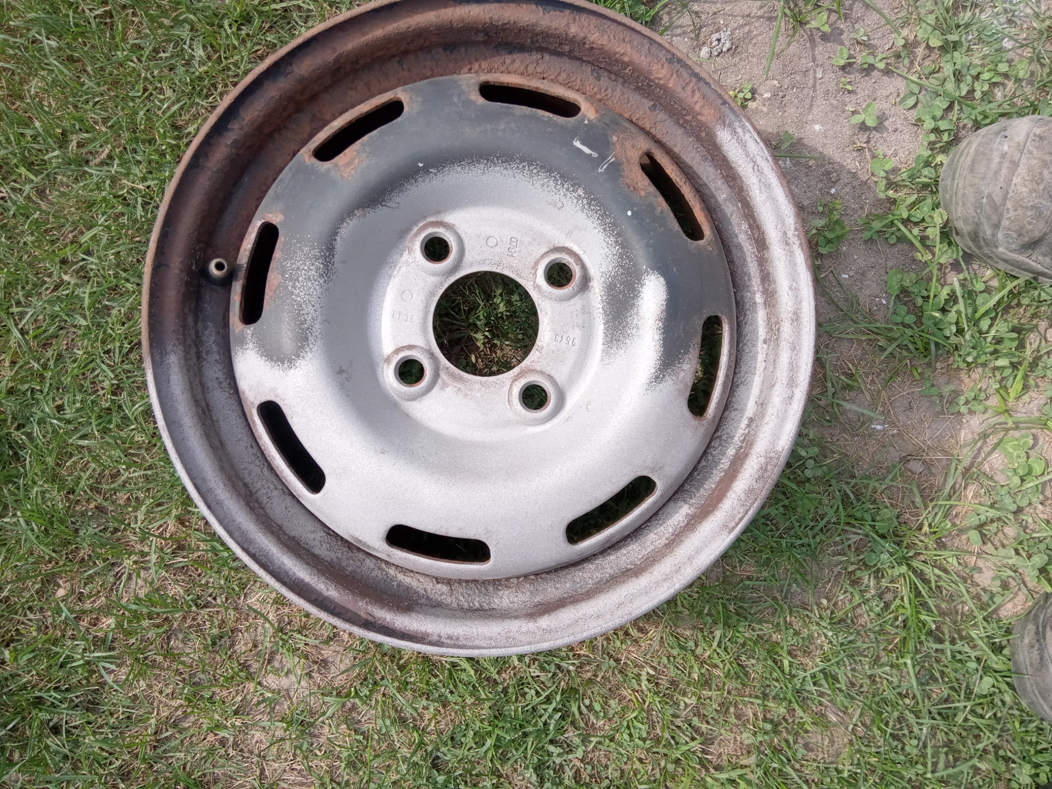 Stara, zardzewiała felga samochodowa leżąca na trawie, z widocznymi śladami korozji i resztkami farby.