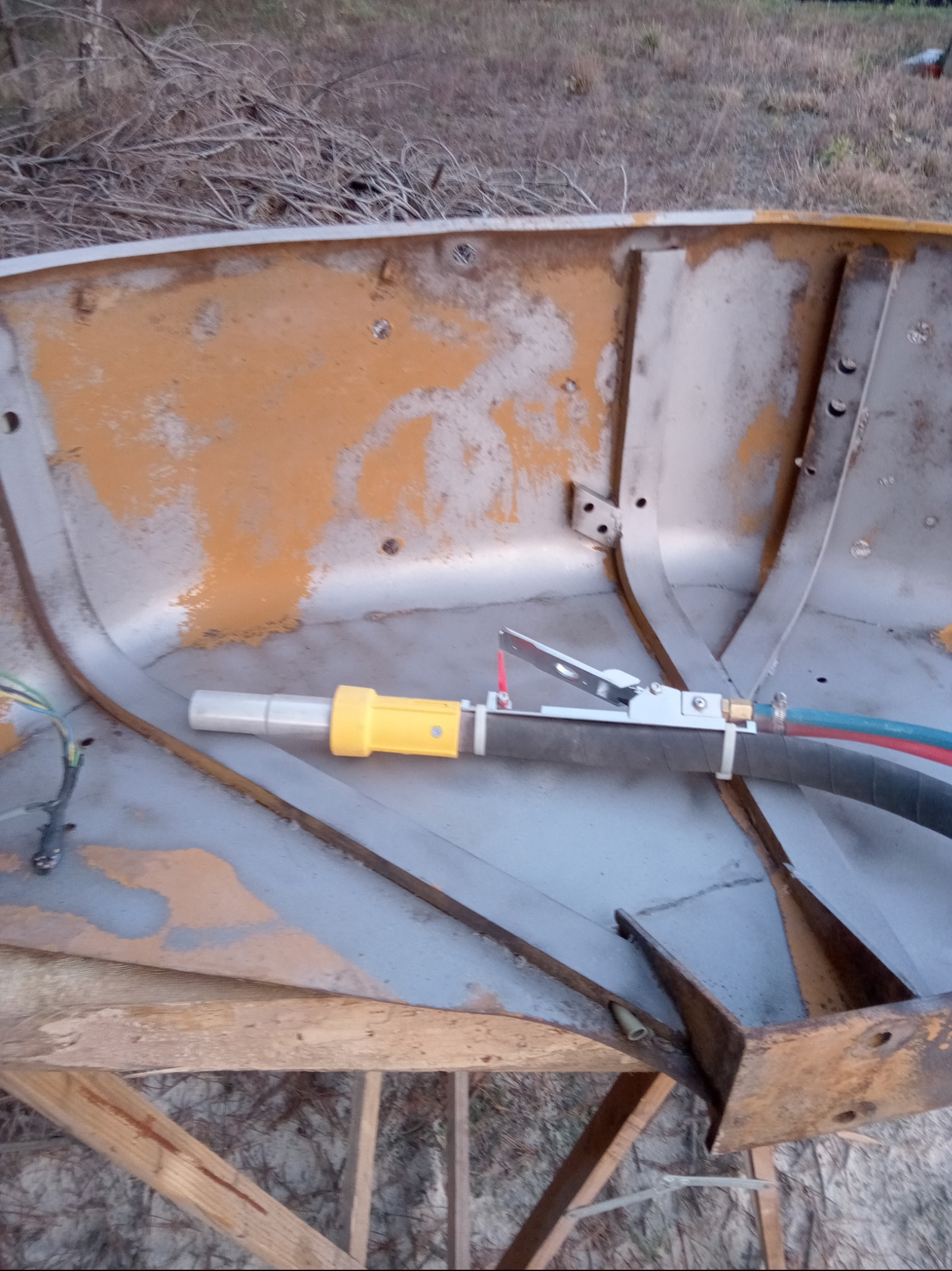 Wnętrze metalowej konstrukcji, częściowo oczyszczonej z rdzy i starej farby metodą piaskowania, widoczny pistolet do piaskowania z żółtą końcówką i przewodami.