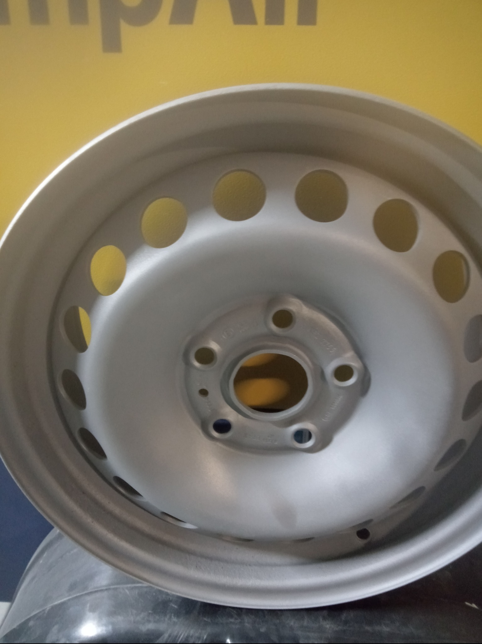 Oczyszczona, metalowa felga samochodowa po obróbce, widoczne otwory wentylacyjne i mocowania śrub, na żółto-niebieskim tle.
