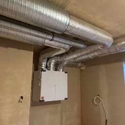 F.H.U Cold&hot - Centrala wentylacyjna z rekuperacją zamontowana na ścianie, z widocznymi przewodami wentylacyjnymi w aluminiowej izolacji, surowy stan wykończenia wnętrza.