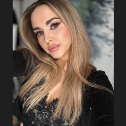 ekiert make up - Portret kobiety z profesjonalnym makijażem oczu i ust, blond włosy opadające na ramiona, czarna bluzka z koronką, delikatne oświetlenie.