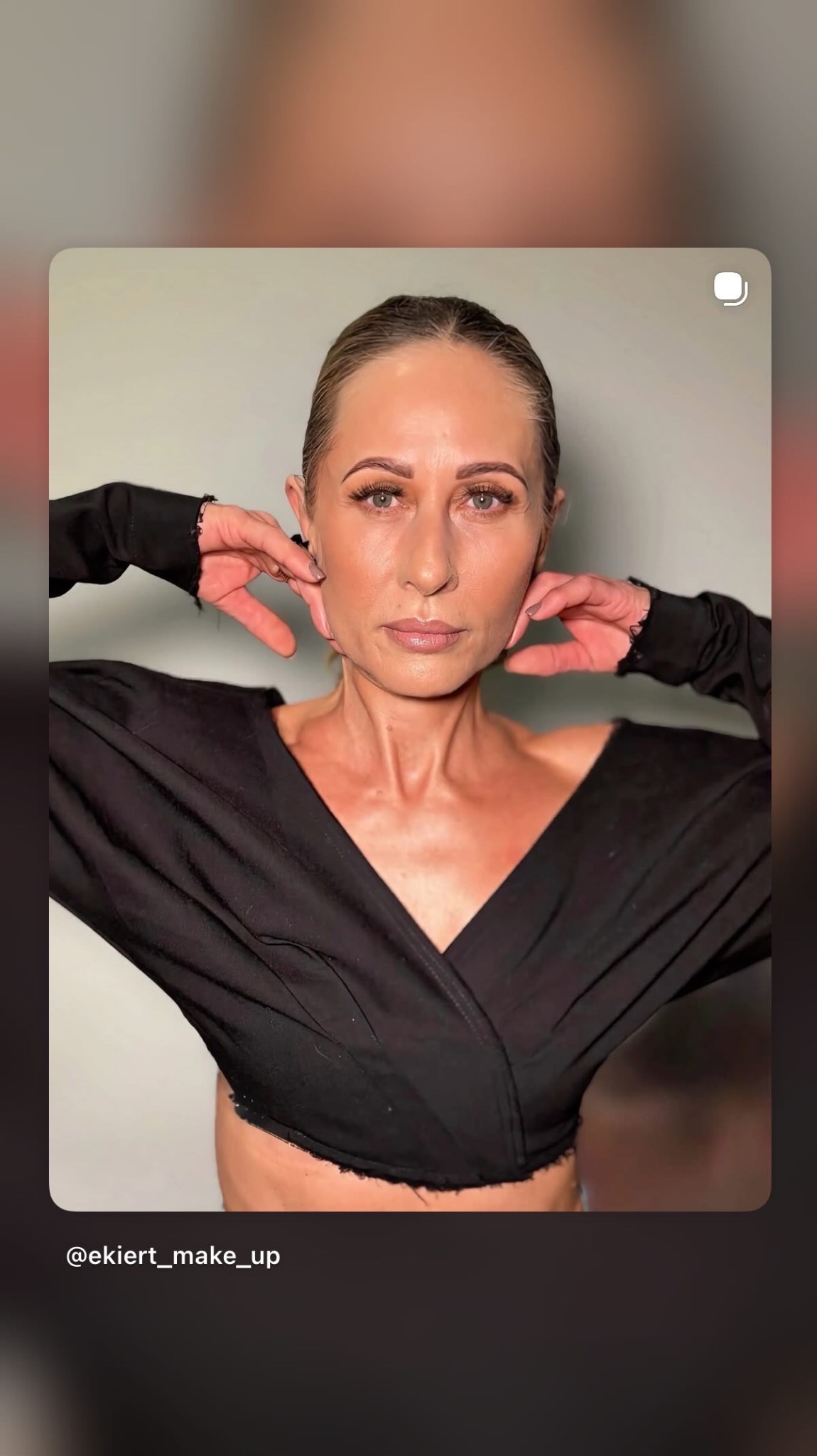 Portret kobiety z delikatnym makijażem, dłonie przy twarzy, czarna bluzka z dekoltem w serek, neutralne tło. Ujęcie z bliska, skupione na twarzy i makijażu.