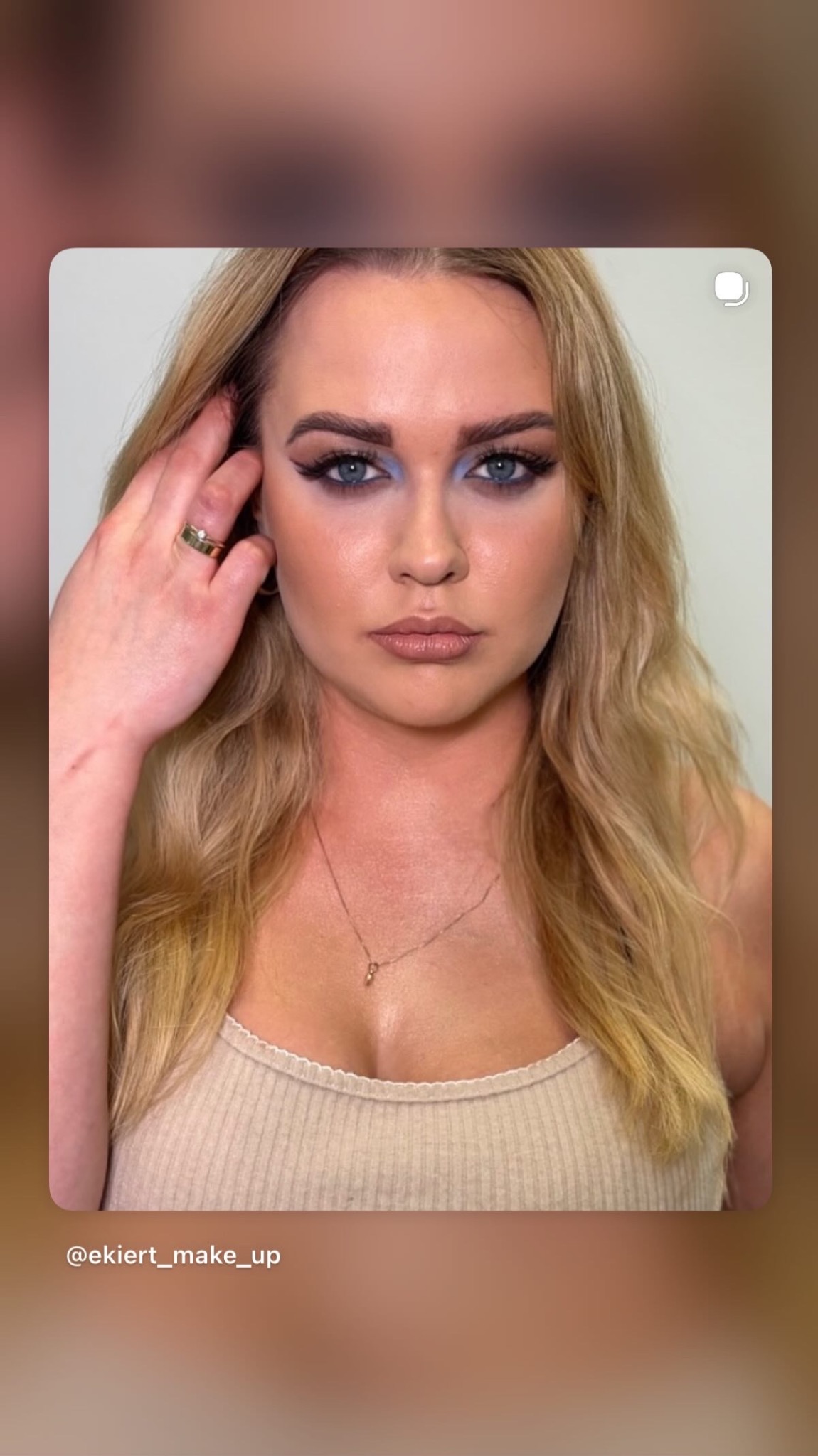 Portret blondynki z intensywnym, niebieskim cieniem do powiek i czarnym eyelinerem. Widoczny złoty pierścionek na palcu i delikatny naszyjnik. Usta w kolorze nude.