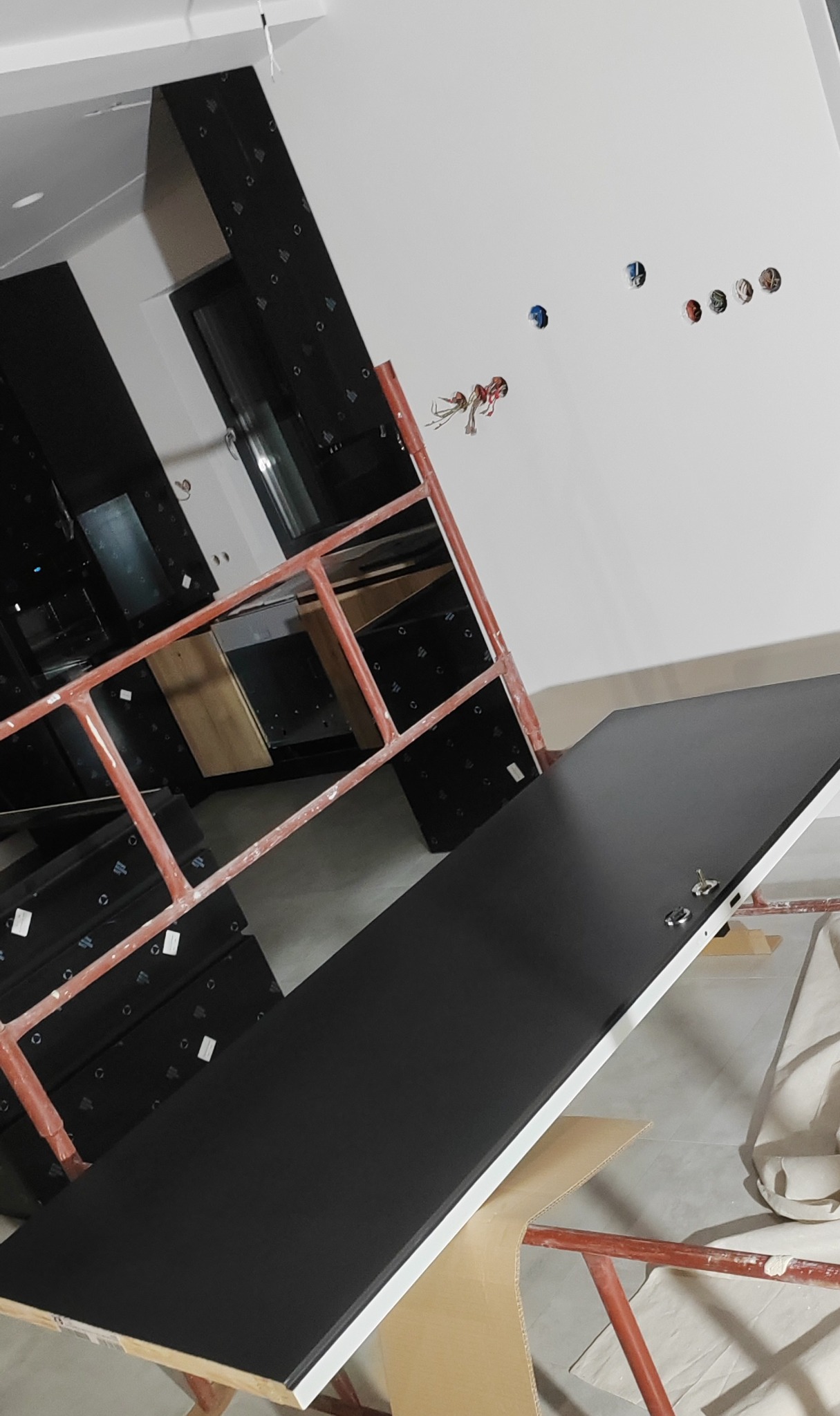 Częściowo zamontowane czarne panele ścienne na rusztowaniu, widoczne otwory na kable w ścianie, przygotowanie do dalszych prac wykończeniowych.