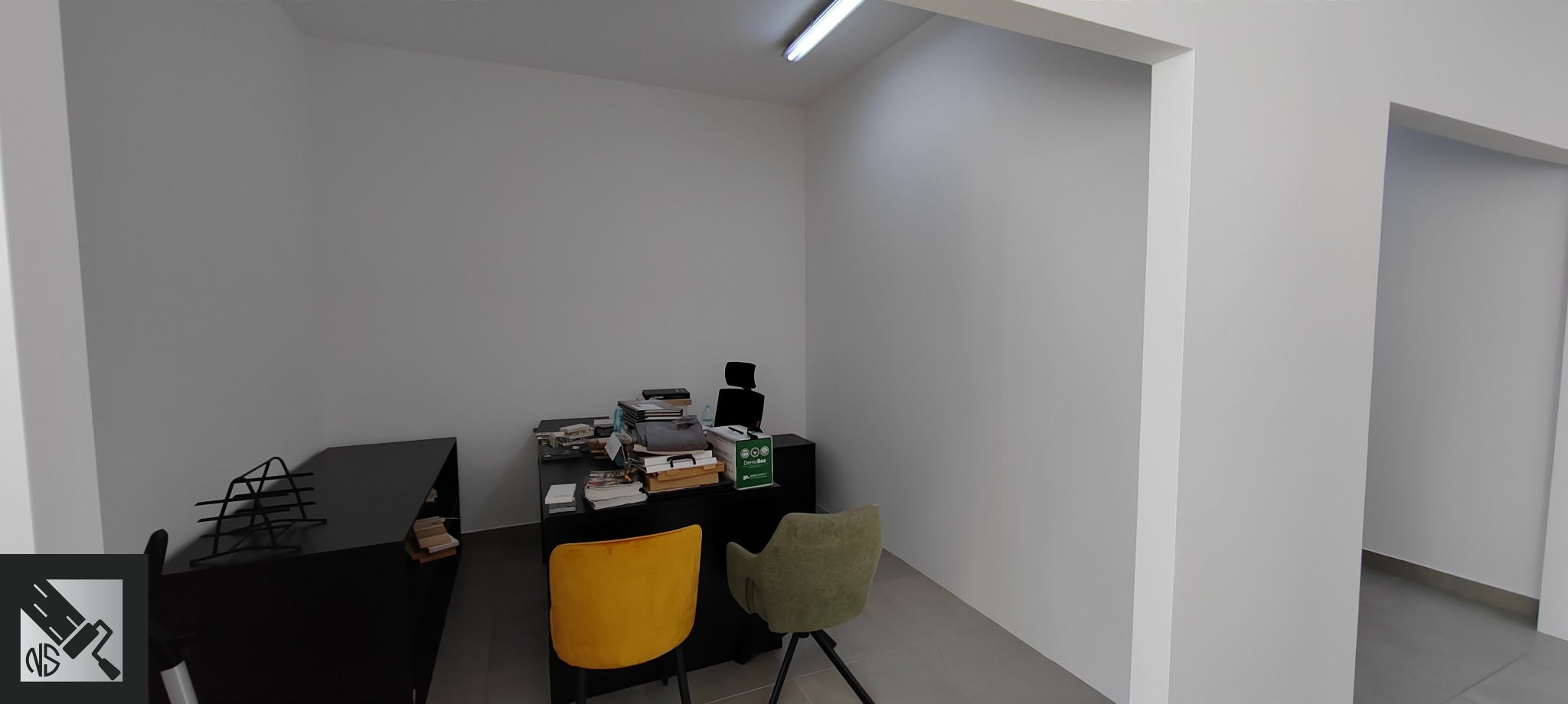 Wnętrze biura po malowaniu ścian na jednolity, jasny kolor, z widocznym biurkiem, krzesłami i lampą sufitową.