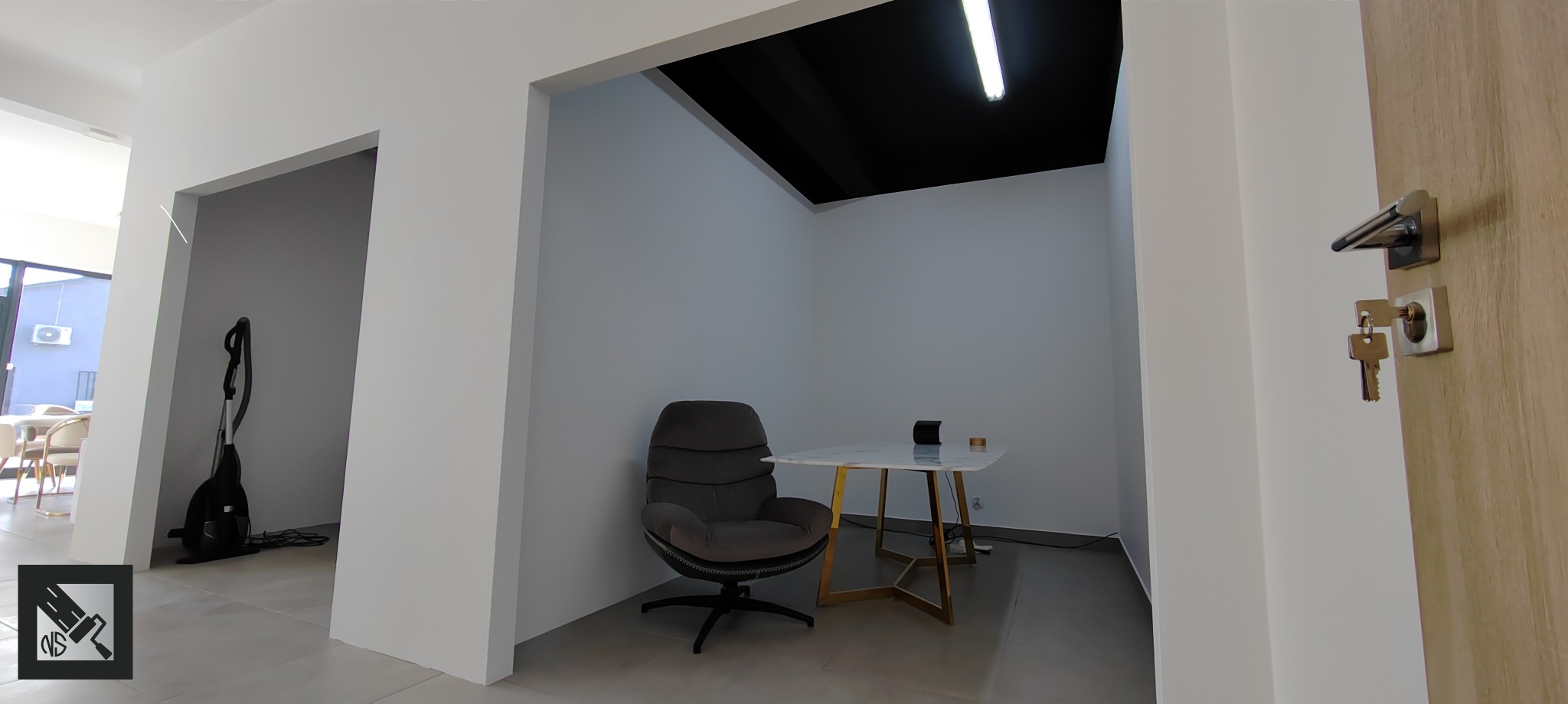 Wnętrze biura po remoncie: świeżo pomalowane, jasne ściany, czarny sufit, designerski fotel i stolik na złotych nogach, widoczny odkurzacz w tle.
