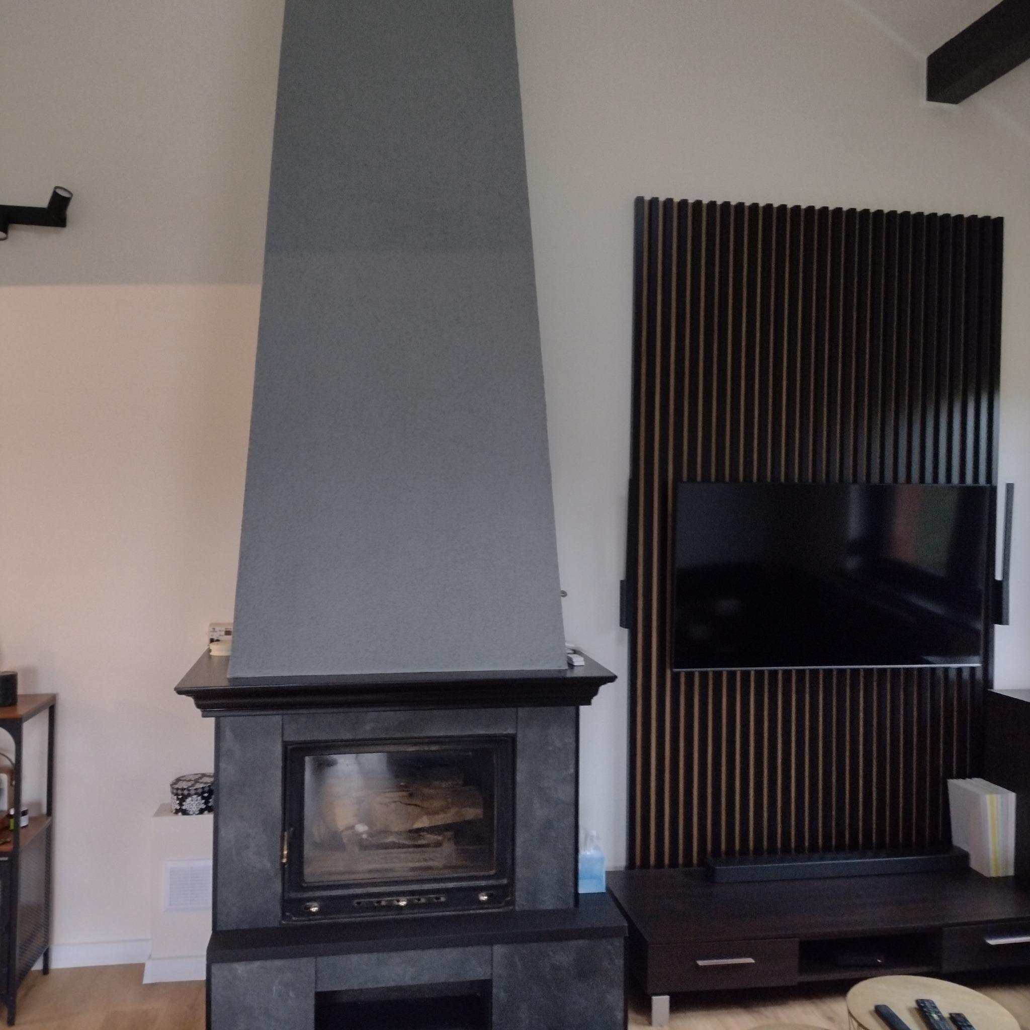 Szary kominek z wkładem i drewnem w nowoczesnym salonie z panelem dekoracyjnym na ścianie