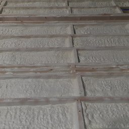 BEKO ARTS izolacje natryskowe pianą pur - Drewniana konstrukcja wypełniona białą pianą izolacyjną, widok z góry, częściowo widoczny przewód doprowadzający pianę.