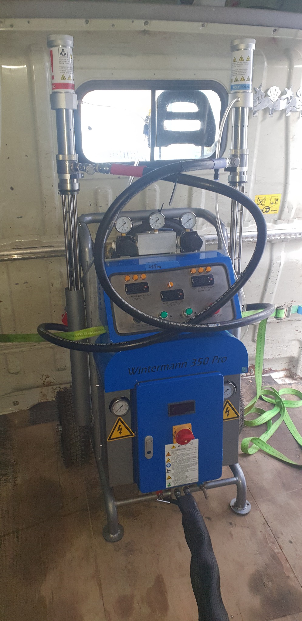 Maszyna Wintermann 350 Pro do natrysku pianki poliuretanowej, widoczna wewnątrz furgonetki, z manometrami, przewodami i zbiornikami na komponenty.